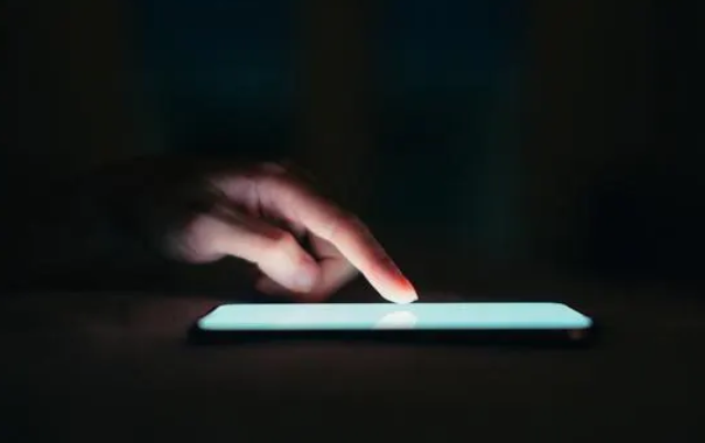An image of someone in a dark room, touching a glowing white phone screen