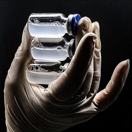 a close photo of a hand in a white nitrile glove holding three vials of foggy white liquid
